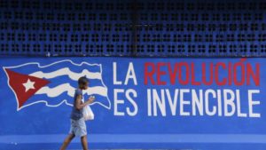 A boy walks past a graffiti reading "The revolution is invincible" in Havana